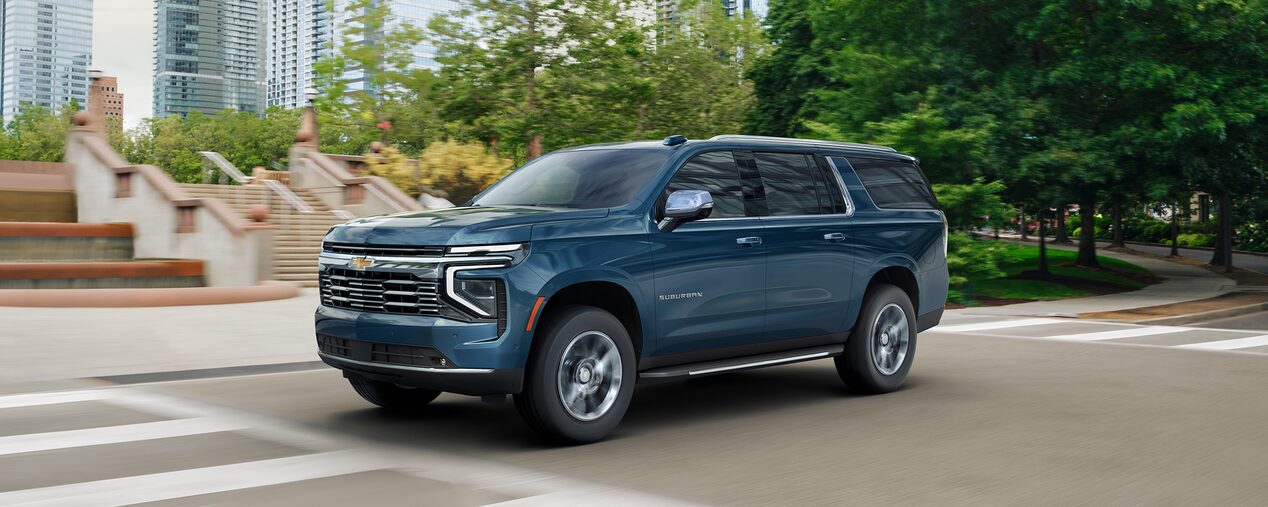 Driving image with front three quarters view of 2025 Chevrolet Suburban Premier  in city surrounded by trees
