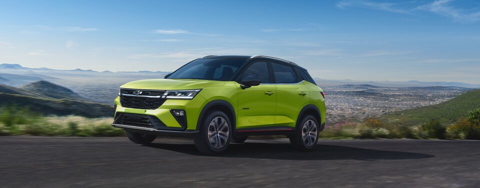 Front Three Quarters of a Green 2026 Chevrolet Groove Driving Down a Mountain Road Overlooking a City Landscape