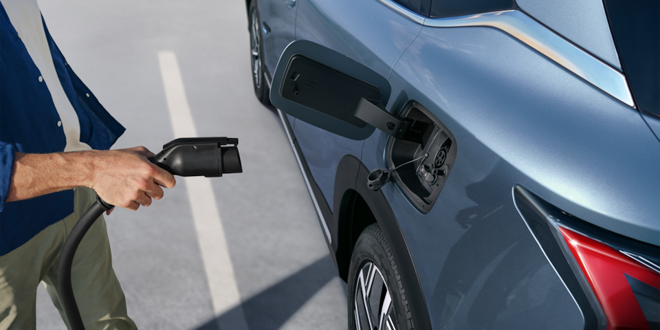 Side view of a man using a charging port on a Dawn Blue 2026 Chevrolet Captiva EV