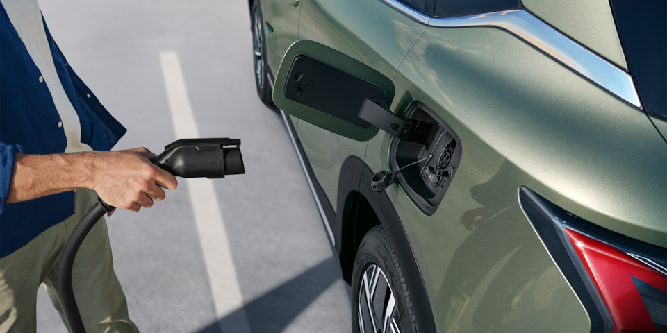 Side view of a man using a charging port on a Khaki Green 2026 Chevrolet Captiva PHEV