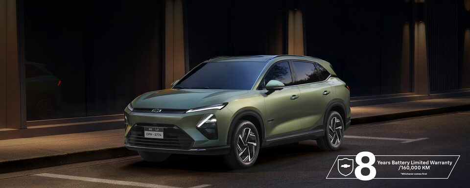 Rear Three Quarters of a Khaki Green 2026 Chevrolet Captiva PHEV Driving Up a Mountain Road Overlooking a City Landscape