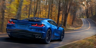 Three Quarters Rear View of a Blue Chevy Corvette E-Ray Driving Down the Road Surrounded by Trees