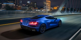 Three Quarters Rear View of a 2025 Blue Chevy Corvette E-Ray Driving Down the Road Under a Night Sky