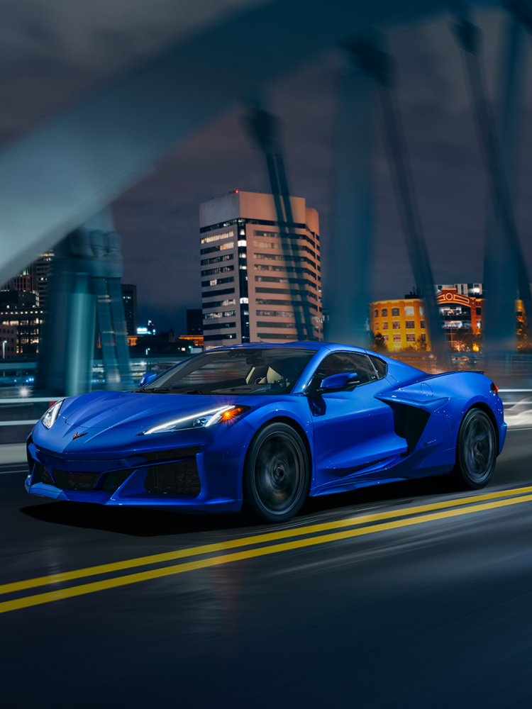 Three Quarters View of a 2025 Blue Chevy Corvette Driving Down the Bridge at Night