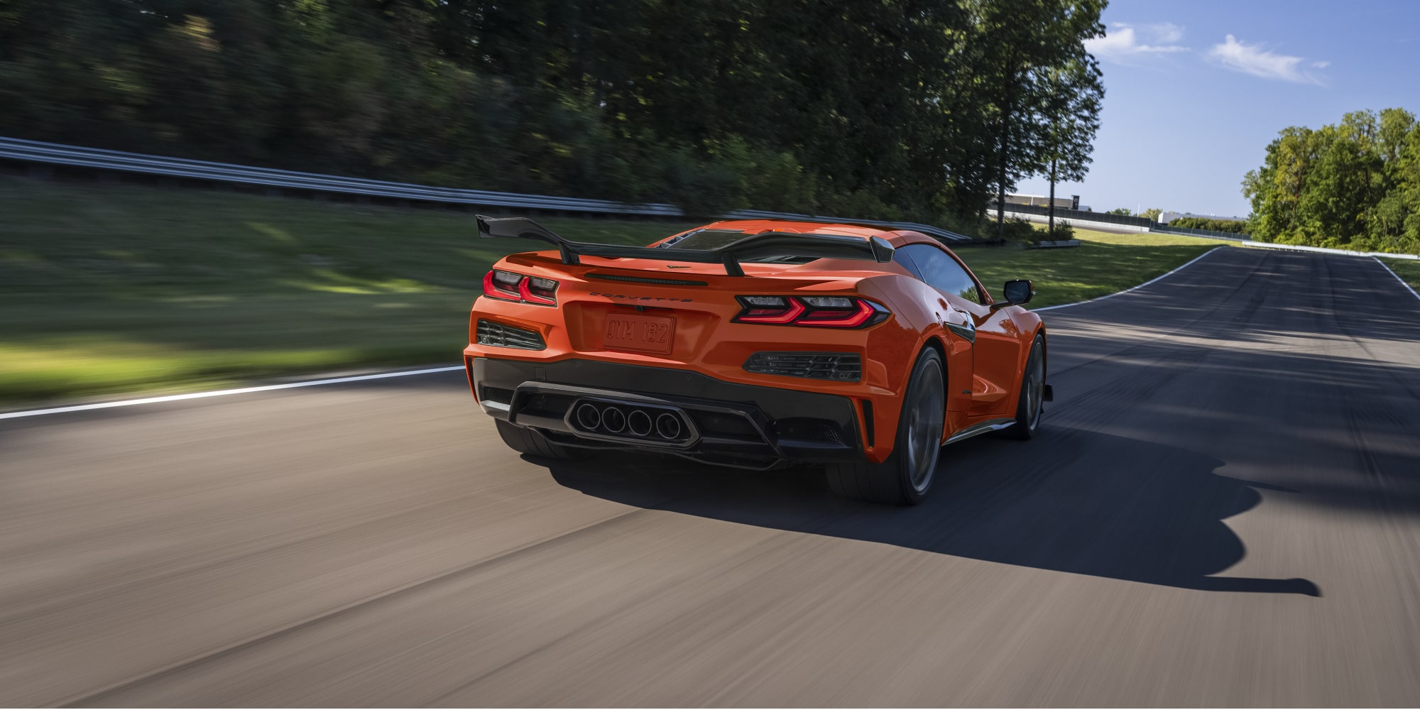 Three Quarters Rear View of an Orange Chevy Corvette Z06 Driving Down the Road on a Sunny Day