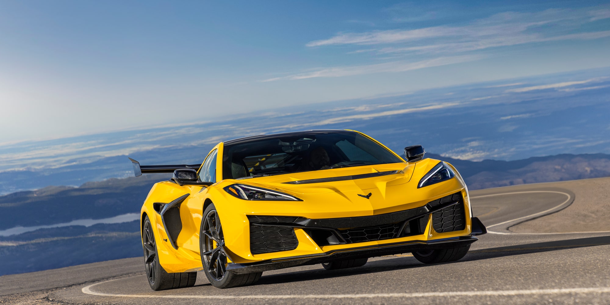 Low Angle Three Quarters View of a Yellow Chevy Corvette ZR1 Going down a Road with a Clear Blue Sky