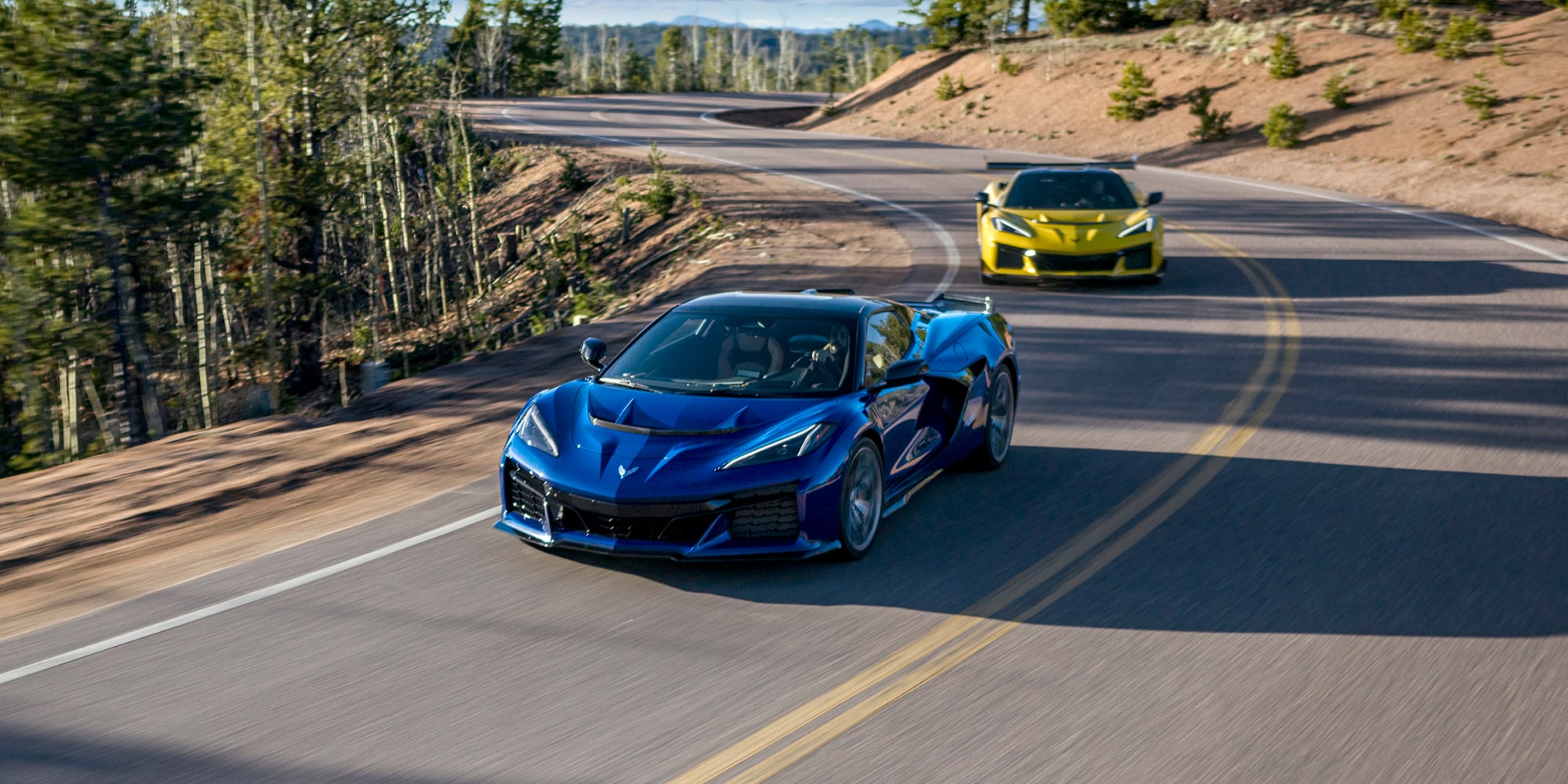 Two Purple and Yellow 2026 Chevy Corvette ZR1 Racing Down a Road under on a Sunny Day