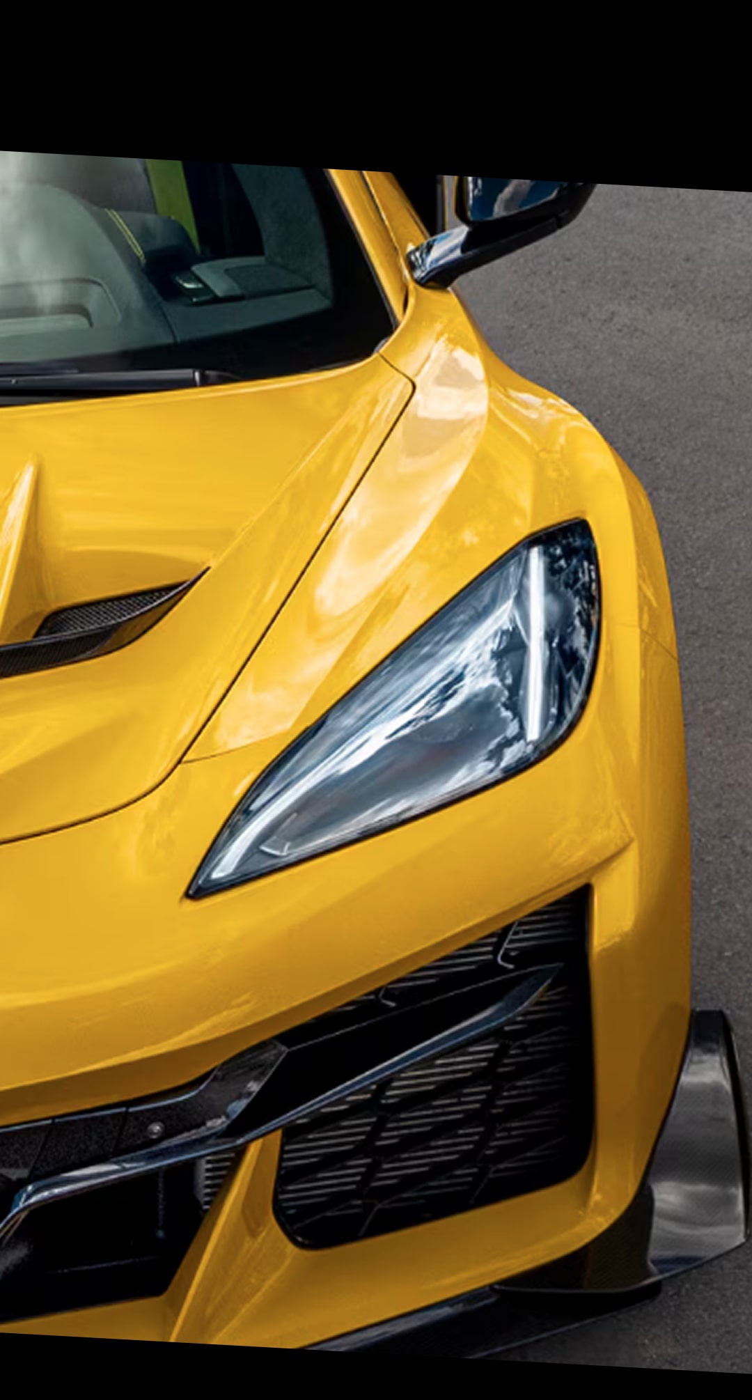 A Close-Up of the Front Corner of a Yellow Chevy Corvette ZR1 Featuring a Sleek Headlight, Sculpted Hood, and Black Lower Grille on a Paved Road.