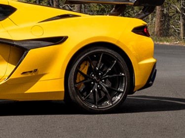 A Close-Up of the Rear Quarter of a Yellow Chevy Corvette ZR1 Featuring a Black Multi-Spoke Wheel, Yellow Brake Caliper, and Sculpted Side Intake Along a Paved Road.
