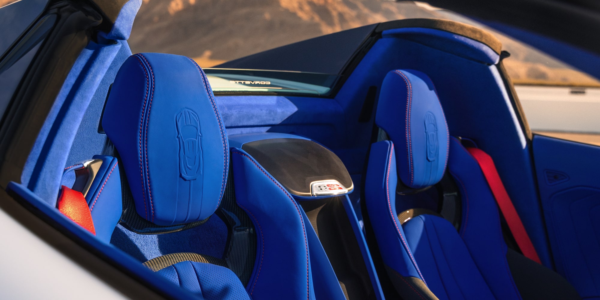 The Blue Leather Seats of a Chevrolet Corvette Grand Sport Convertible Are Shown in Bright Sunlight With Mountains Visible in the Background.