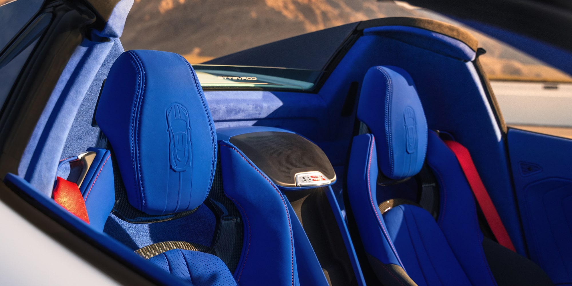 The Blue Leather Seats of a Chevrolet Corvette Grand Sport Convertible Are Shown in Bright Sunlight With Mountains Visible in the Background.