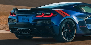 The Rear of a Blue Chevrolet Corvette Grand Sport With Red Accent Stripes and Quad Exhaust Outlets Is Shown Driving Along a Sunlit Racetrack.
