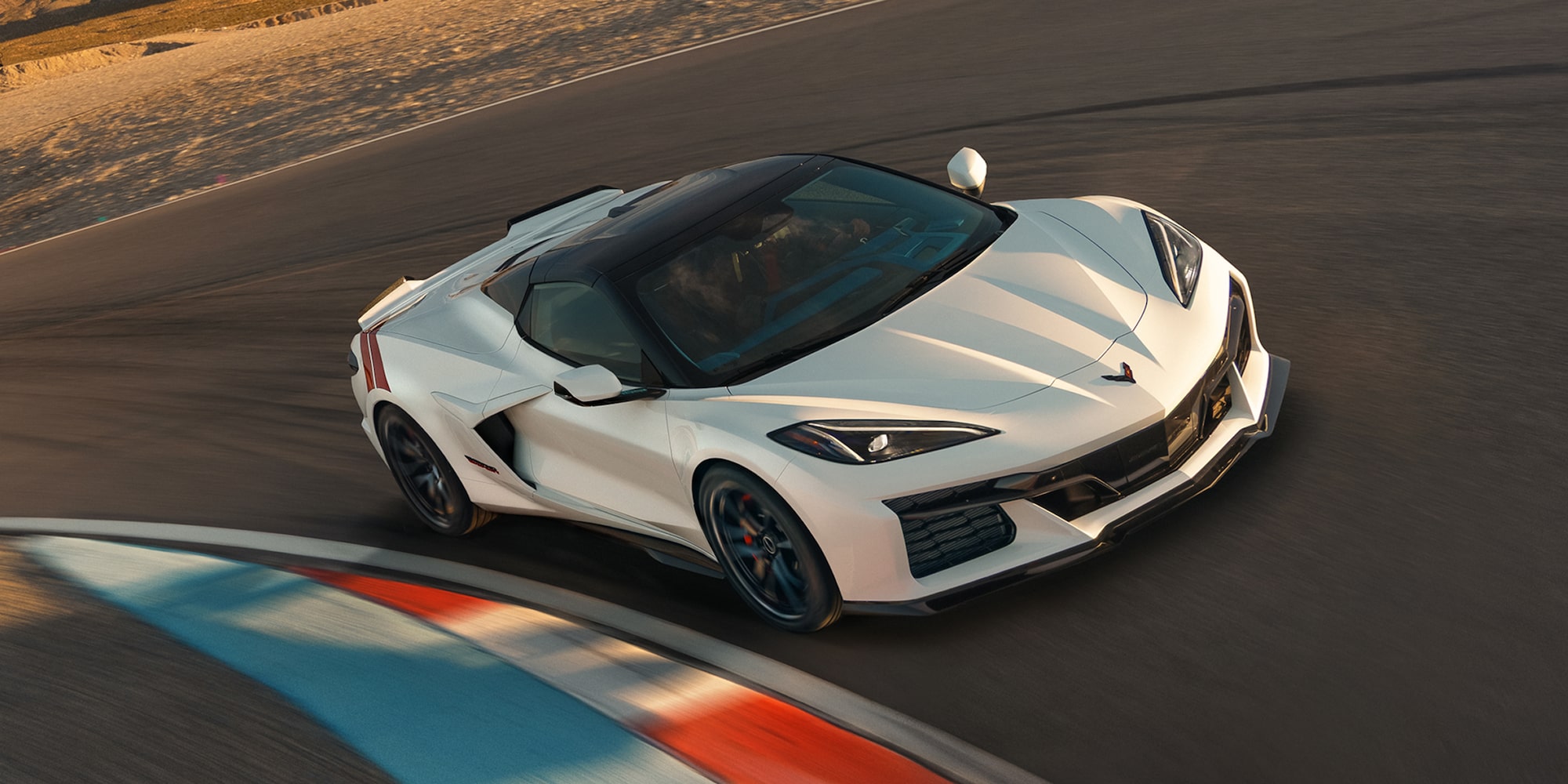 A White Chevrolet Corvette Grand Sport With Red Accent Stripes Leans Into a Curved Racetrack Section With Motion Blur Across the Painted Apex.