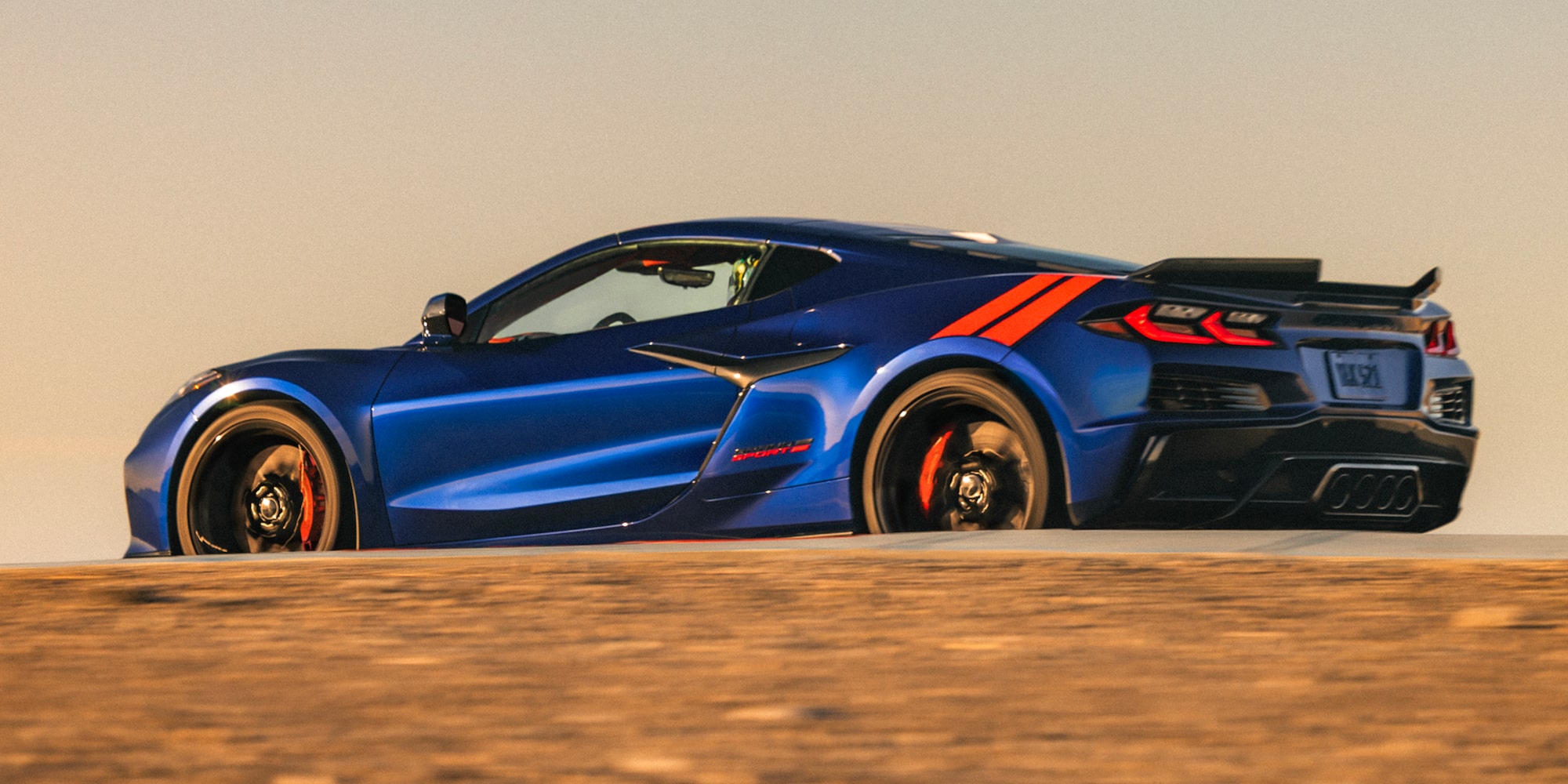 A Blue Chevrolet Corvette Grand Sport Drives Across a Sunlit Dirt Surface With Motion Blur and Warm Golden‑Hour Lighting.