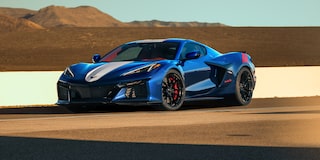 A Blue Chevrolet Corvette Grand Sport With Red Accent Stripes Drives Along a Racetrack Beside a White Barrier Under Warm Sunlight.
