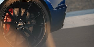 A Close‑Up Shot Shows the Black Wheel and Red Brake Caliper of a Blue Chevrolet Corvette Grand Sport Spinning on a Sunlit Racetrack.
