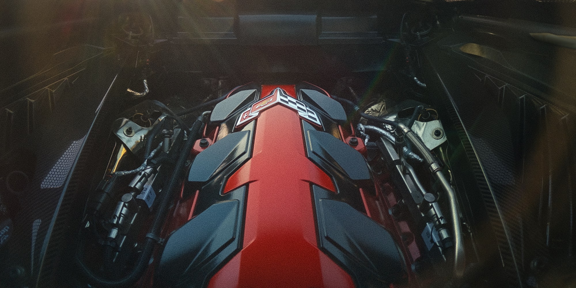 The Engine Bay of a Chevrolet Corvette Grand Sport Shows a Prominent Red Engine Cover Surrounded by Metallic and Black Components Under Soft Sunlight.