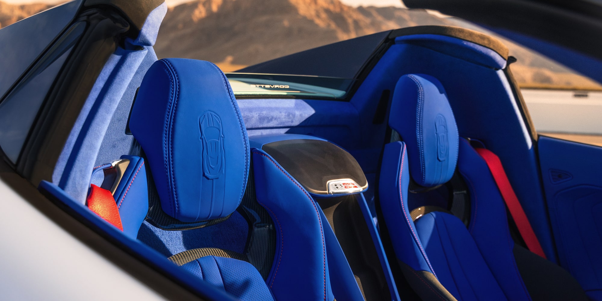 The Blue Leather Seats of a Chevrolet Corvette Grand Sport Convertible Are Shown in Bright Sunlight With Mountains Visible in the Background.