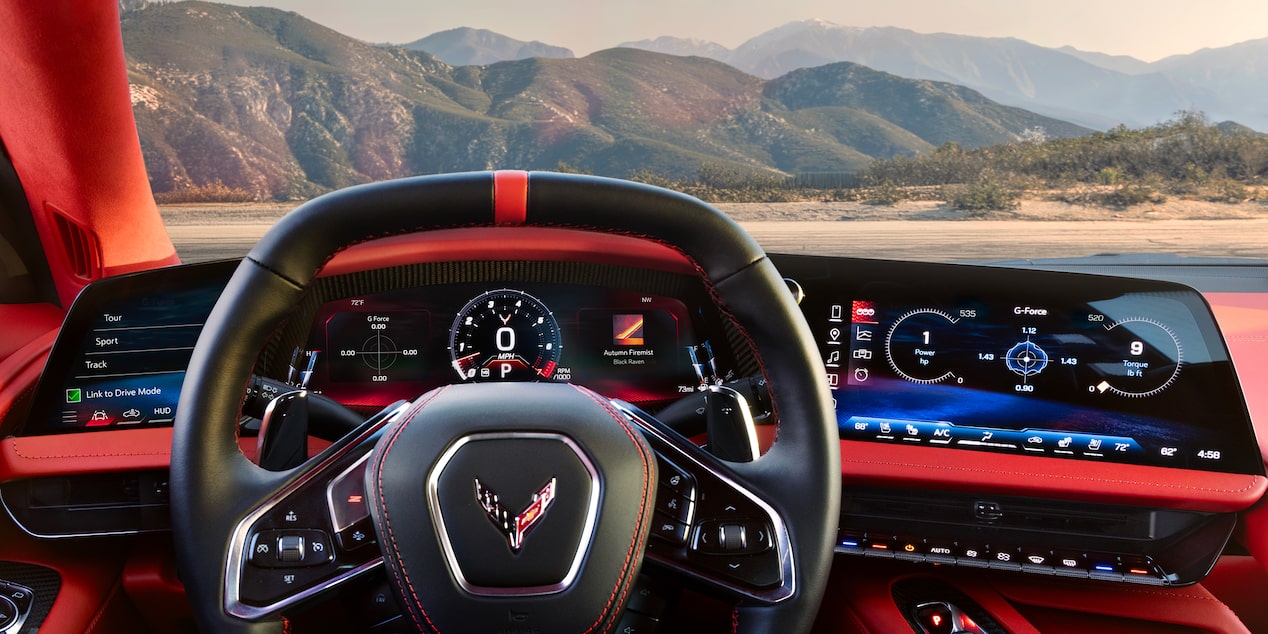 The Driver’s View Inside a Chevrolet Corvette Grand Sport Shows the Steering Wheel, Digital Displays, and a Mountain Landscape Visible Through the Windshield.