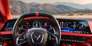 The Driver’s View Inside a Chevrolet Corvette Grand Sport Shows the Steering Wheel, Digital Displays, and a Mountain Landscape Visible Through the Windshield.