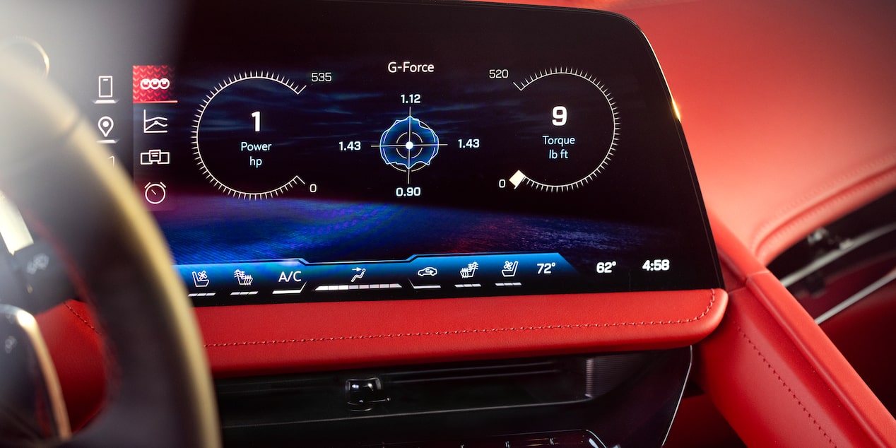 A Close‑Up of the Central Digital Display in a Chevrolet Corvette Grand Sport Shows Performance Readouts and Infotainment Controls Against the Red Interior Trim.