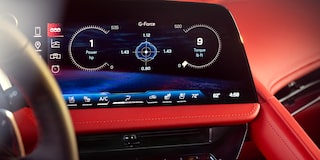 A Close‑Up of the Central Digital Display in a Chevrolet Corvette Grand Sport Shows Performance Readouts and Infotainment Controls Against the Red Interior Trim.
