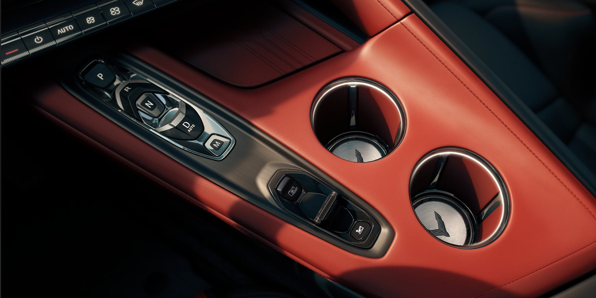 A Close‑Up View of the Center Console in a Chevrolet Corvette Grand Sport Shows Metallic Switch Controls Beside Two Circular Cupholders Set in Red Interior Trim.