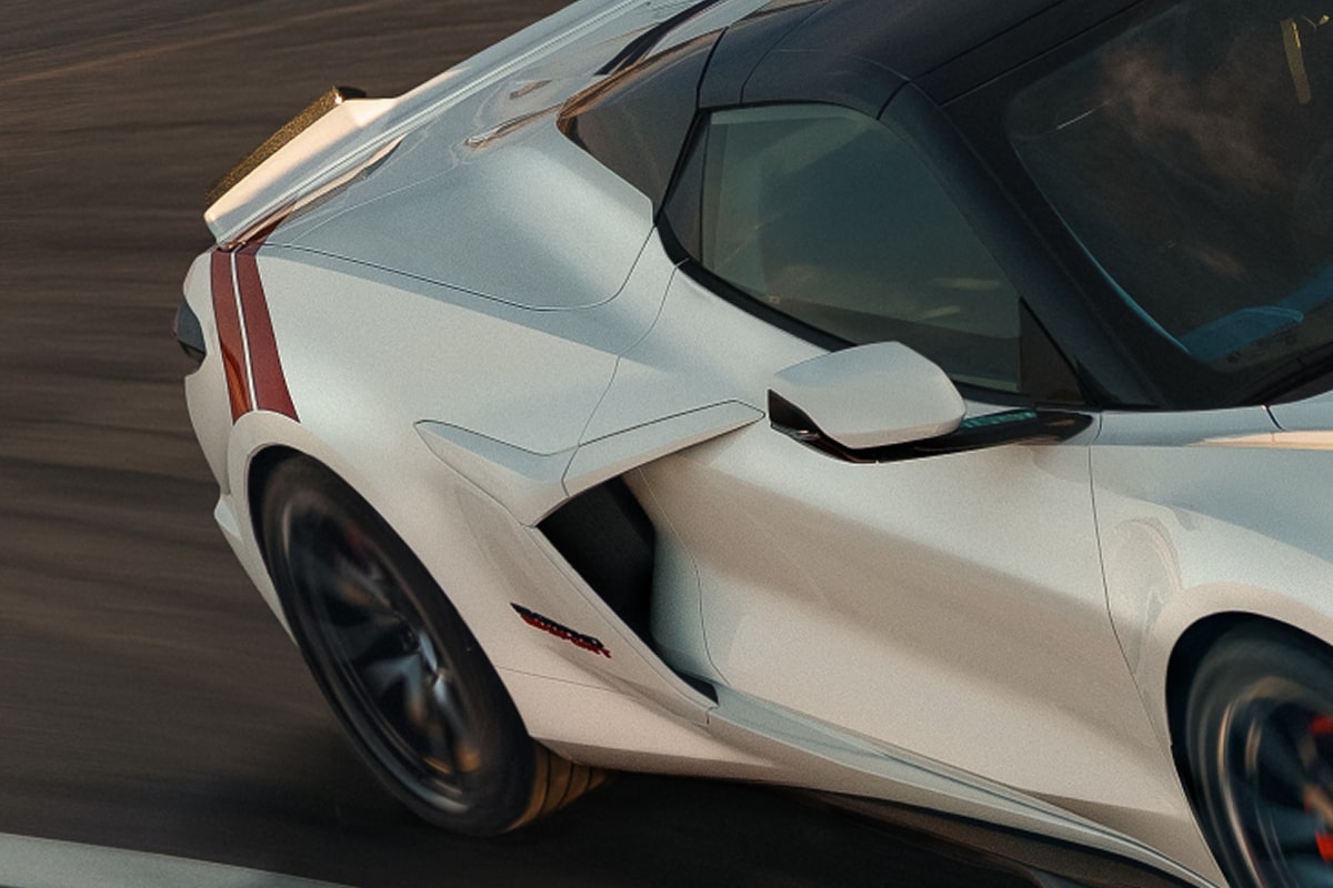 A White Chevrolet Corvette Grand Sport Speeds Through a Sunlit Corner, Showing Its Sculpted Side Air Intake, Black Wheels, and Red Accent Stripes.