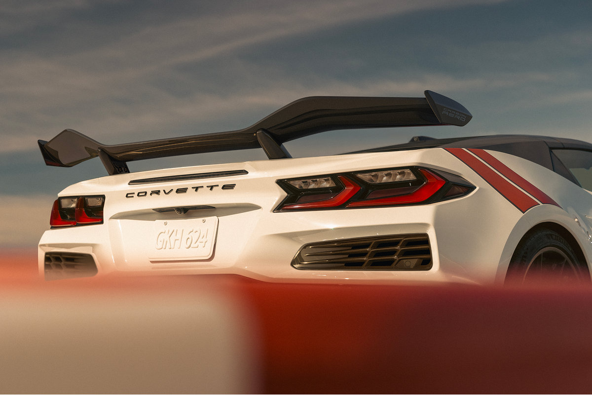 A White Chevrolet Corvette Grand Sport Speeds Through a Sunlit Corner, Showing Its Sculpted Side Air Intake, Black Wheels, and Red Accent Stripes.
