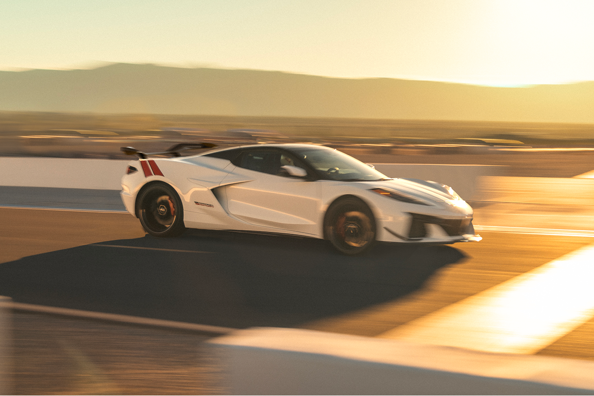 A White Chevrolet Corvette Grand Sport Drives Along a Racetrack at Sunset With Motion Blur Across the Asphalt and Surrounding Landscape.