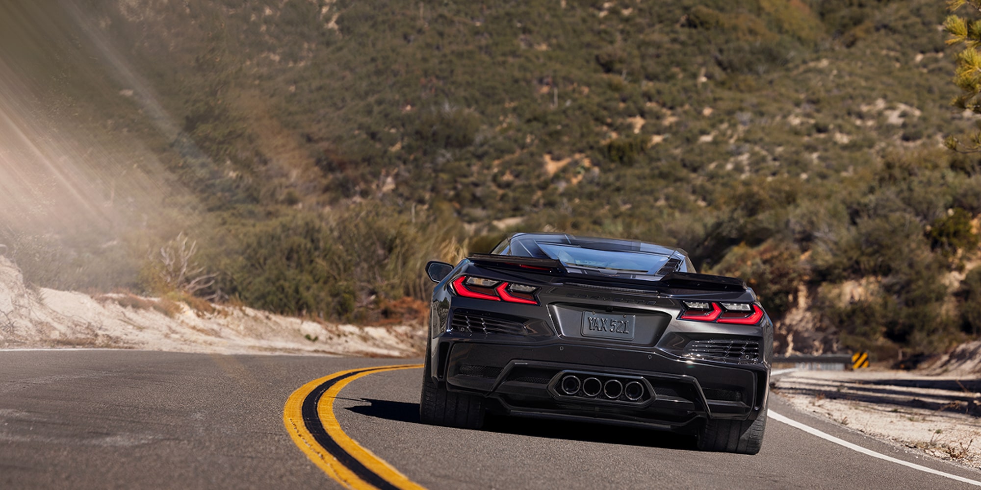 Rear View of a Black Chevrolet Corvette Grand Sport Driving the Curve of a Mountain Road