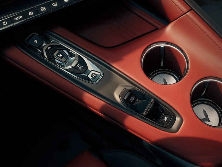 A Close‑Up View of the Center Console in a Chevrolet Corvette Grand Sport Shows Metallic Switch Controls Beside Two Circular Cupholders Set in Red Interior Trim.