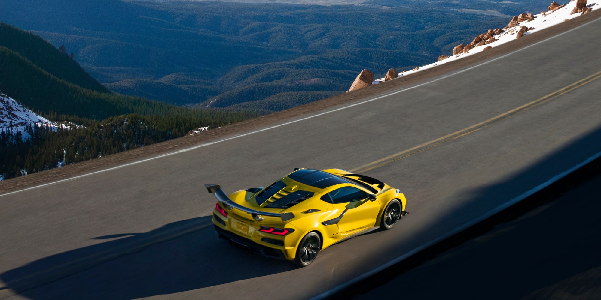 Vista en primer plano del cofre delantero de un Chevrolet Corvette Grand Sport azul en el que se ven franjas de carreras blancas y el emblema de Corvette bañados por la cálida luz del sol.