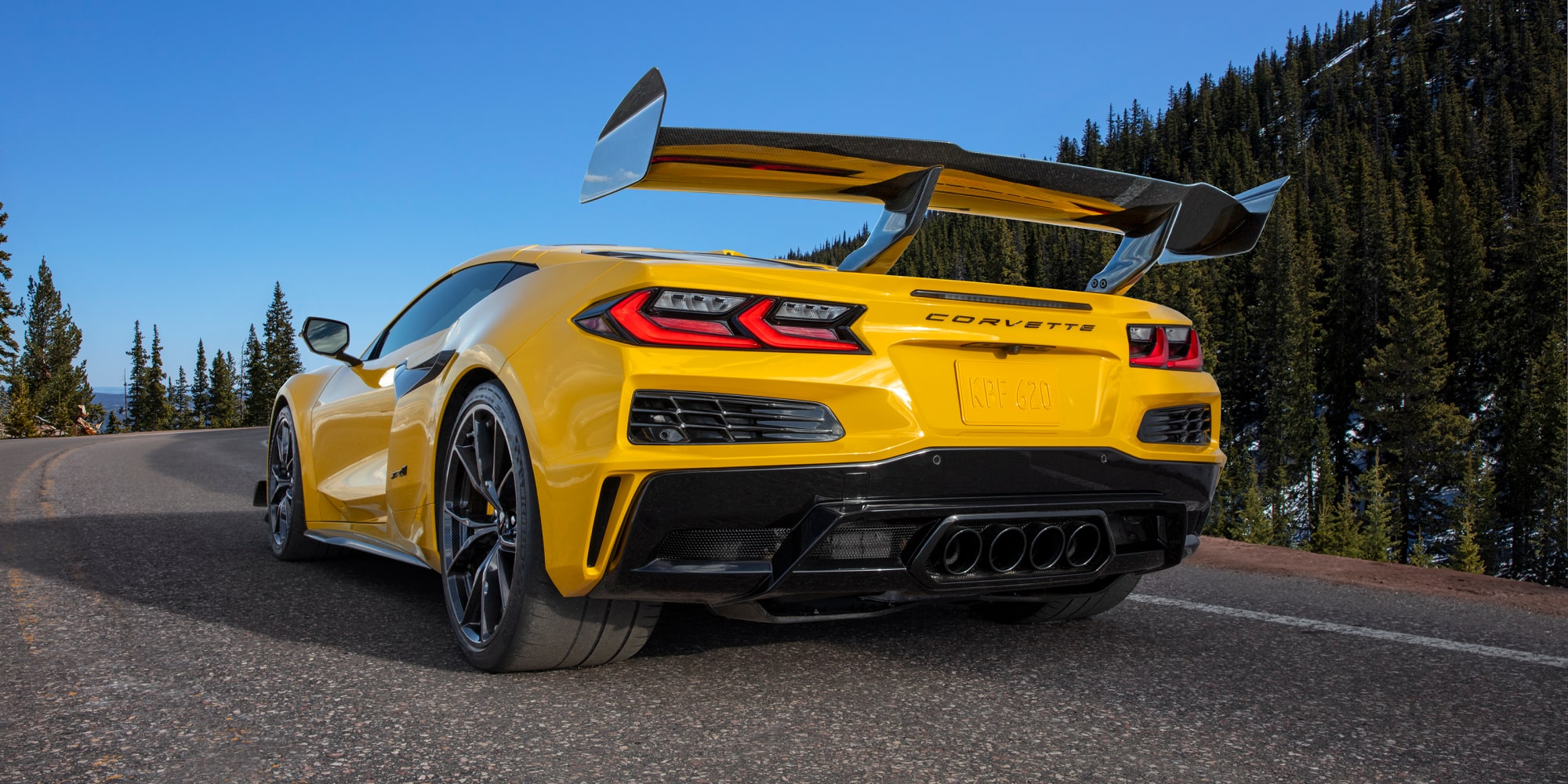 Vista en primer plano del cofre delantero de un Chevrolet Corvette Grand Sport azul en el que se ven franjas de carreras blancas y el emblema de Corvette bañados por la cálida luz del sol.