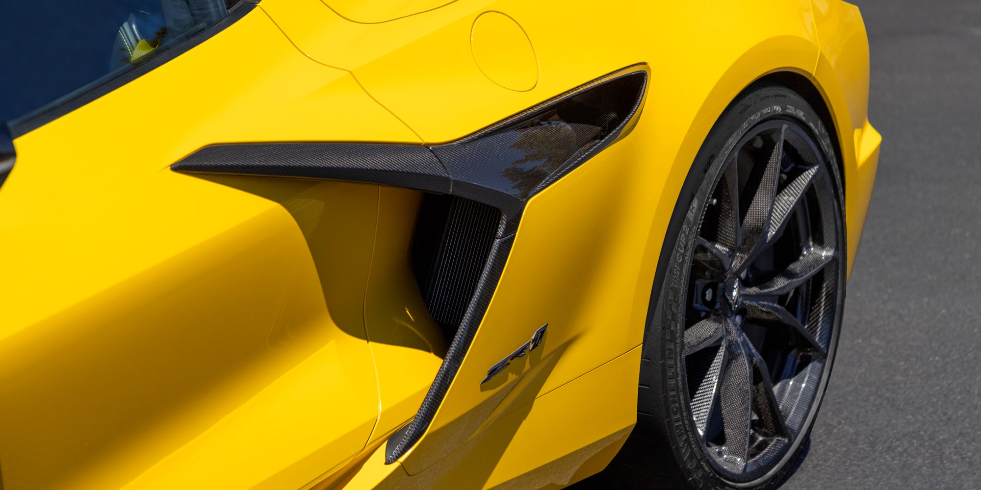 Un Chevrolet Corvette Grand Sport azul circulando por una superficie de tierra iluminada por el sol, con efecto de movimiento e iluminación cálida del atardecer.