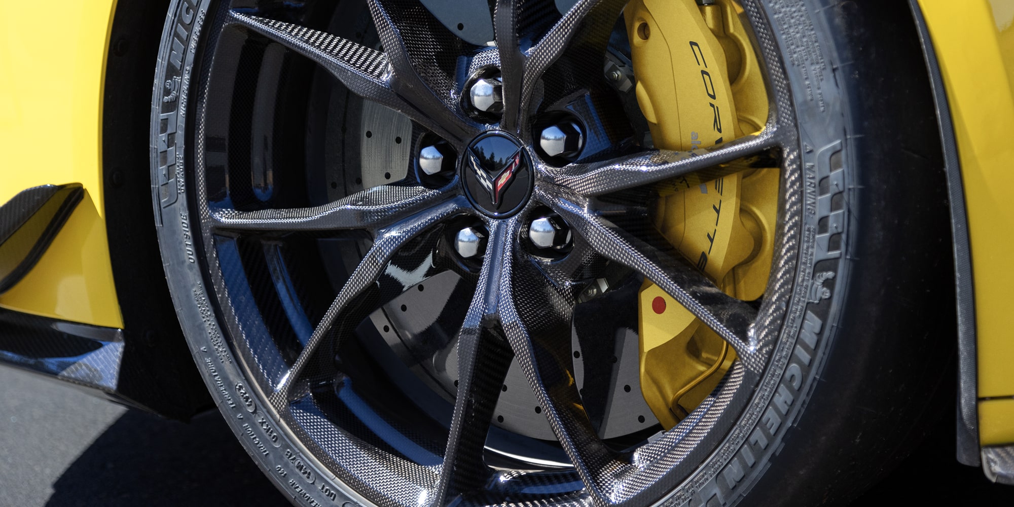 A Close-Up of a Black Multi-Spoke Performance Wheel on a Yellow Chevy Corvette ZR1 Featuring a Large Brake Rotor and Yellow Brake Caliper.