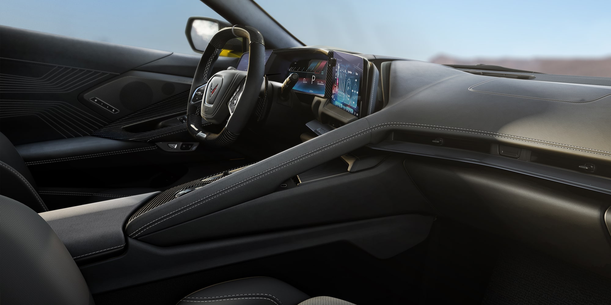 Vista del conductor en el interior de un Chevrolet Corvette Grand Sport, en la que se ven el volante, las pantallas digitales y un paisaje de montaña a través del parabrisas.