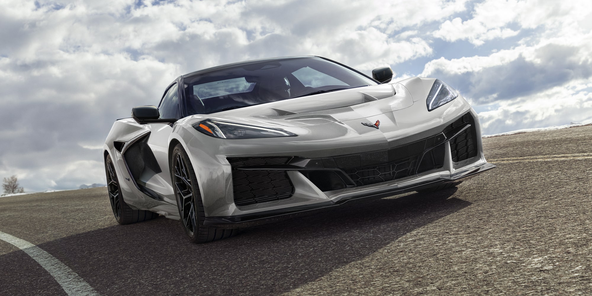 A Blue Chevrolet Corvette Grand Sport With White Racing Stripes Is Parked in a Sunlit Asphalt Lot With Shadows Cast Across the Ground.