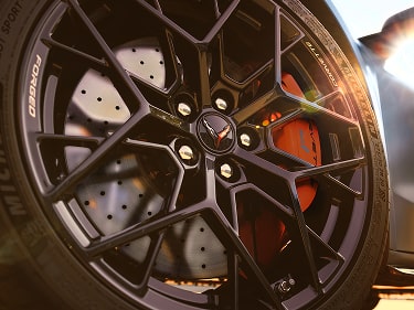 A Close-Up of a Black Multi-Spoke Performance Wheel on the Chevy Corvette ZR1X Featuring Cross-Drilled Brake Rotors, a Red Brake Caliper, and a Corvette Center Cap.