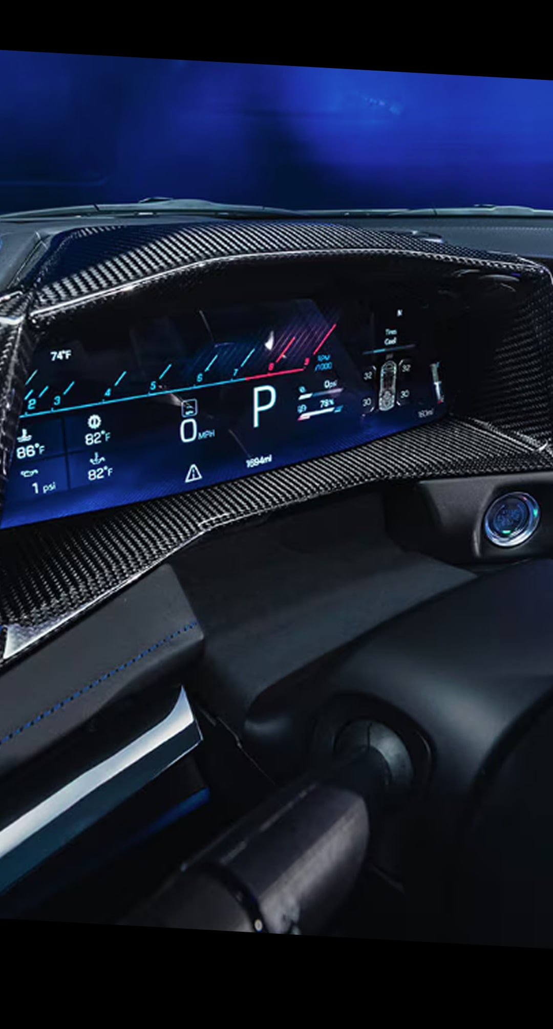 A Close-Up of a Digital Driver Display Inside the Chevy Corvette ZR1X Showing a Curved Screen with Driving Information, a Central Tachometer, and Carbon Fiber Trim with Blue Ambient Lighting.