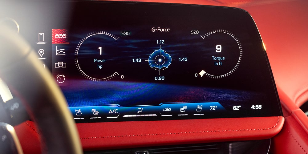 A Close-Up of a Digital Instrument Cluster Inside the Chevy Corvette ZR1X Displaying Driving Information on a Wide Screen with Blue Graphics and a Red Dashboard Surround.