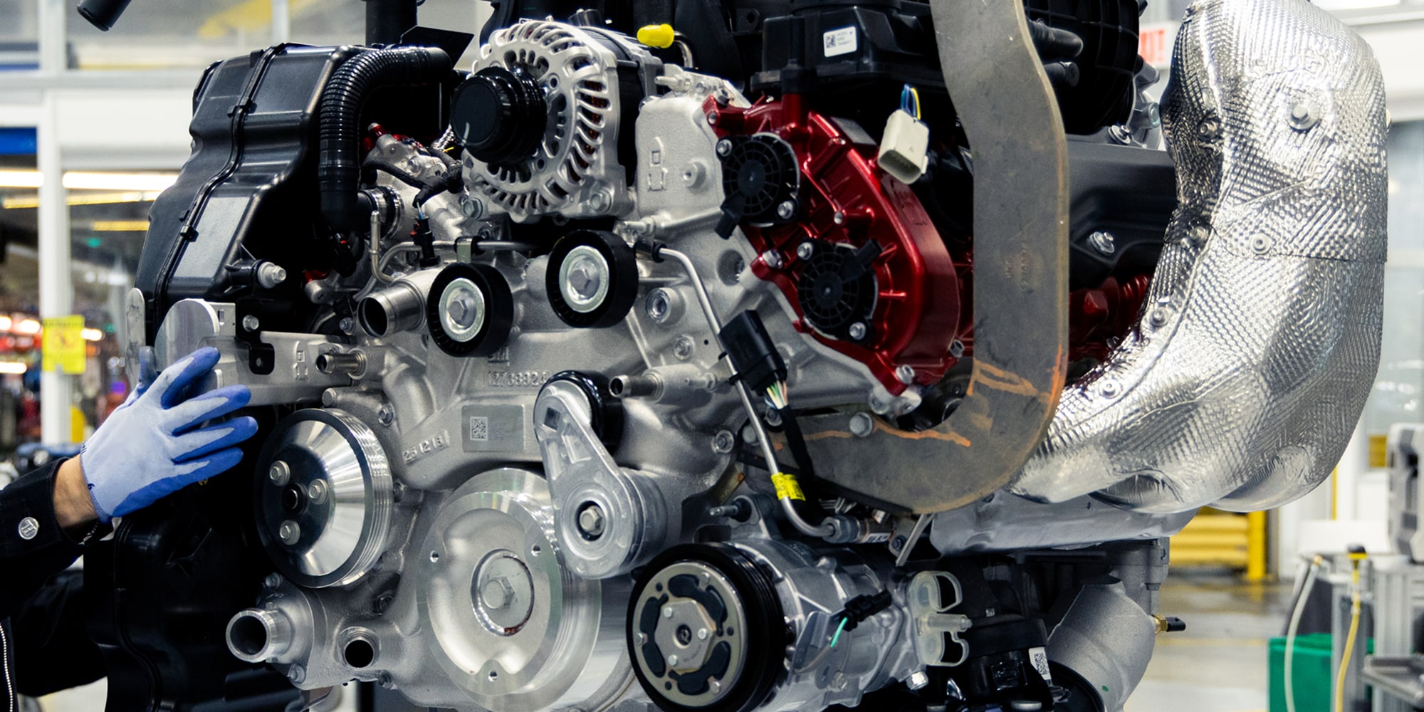 A Gloved Worker Assembles a Chevy Engine With Exposed Metal Components and Hoses on a Factory Assembly Line.