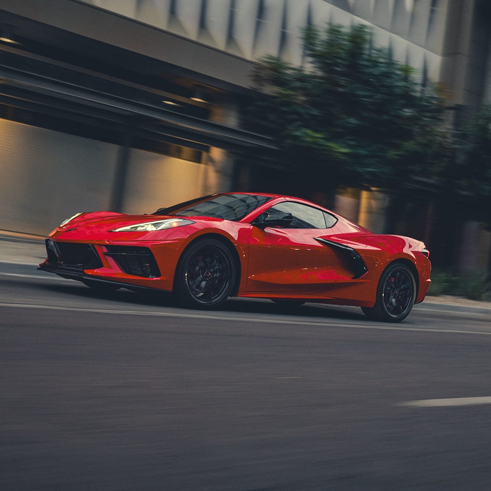 A Wide View of a Red Chevy Corvette Stingray Driving Past a Downtown Building