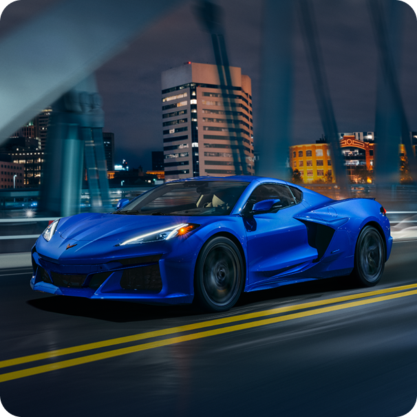 A Wide View of a Blue Chevy Corvette E-Ray Driving on a Bridge Outlooking a Downtown City