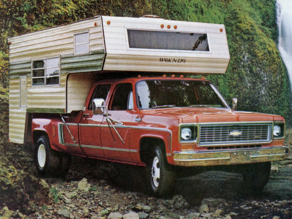 Una foto del folleto de camionetas Chevy del 1973 original con una pickup de la serie C/K roja con casilla en la caja, estacionada en un área boscosa cerca de una cascada. Al lado de la camioneta se ve a un hombre y cuatro muchachos de diferentes edades sentados y de pie.