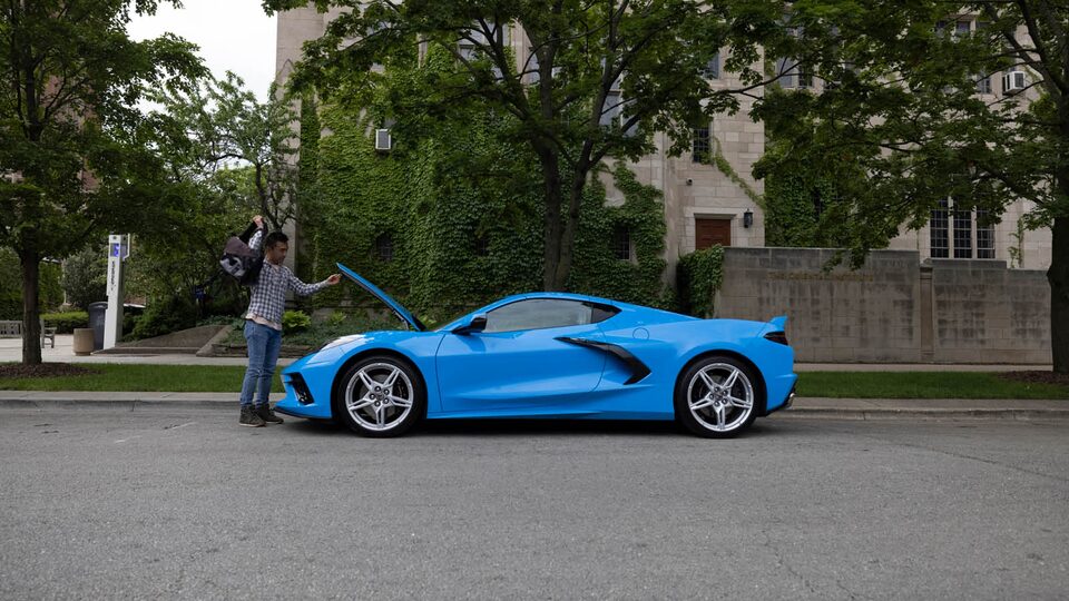 Ken Kuevibulvanich removes a bag from the hood storage area of his 2020 Corvette as it sits on a tree-lined street.