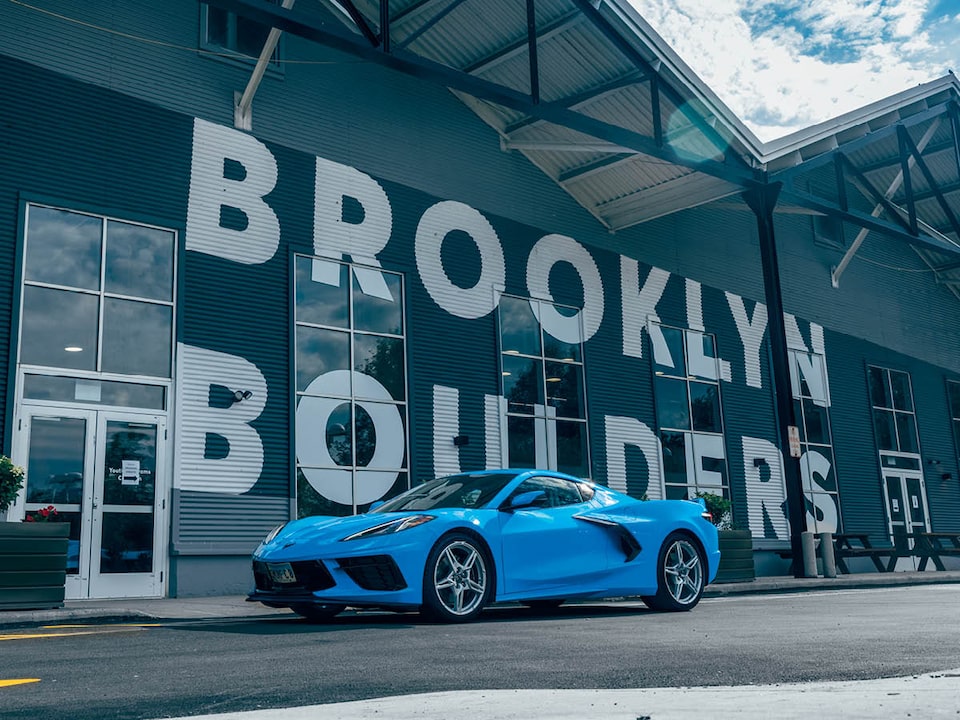 A bright blue 2020 Corvette sits on the street in front of a rock climbing gym with the name “Brooklyn Boulders” in huge white letters on the front of the building.