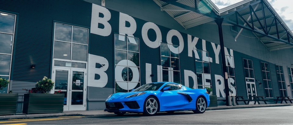 A bright blue 2020 Corvette sits on the street in front of a rock climbing gym with the name “Brooklyn Boulders” in huge white letters on the front of the building.