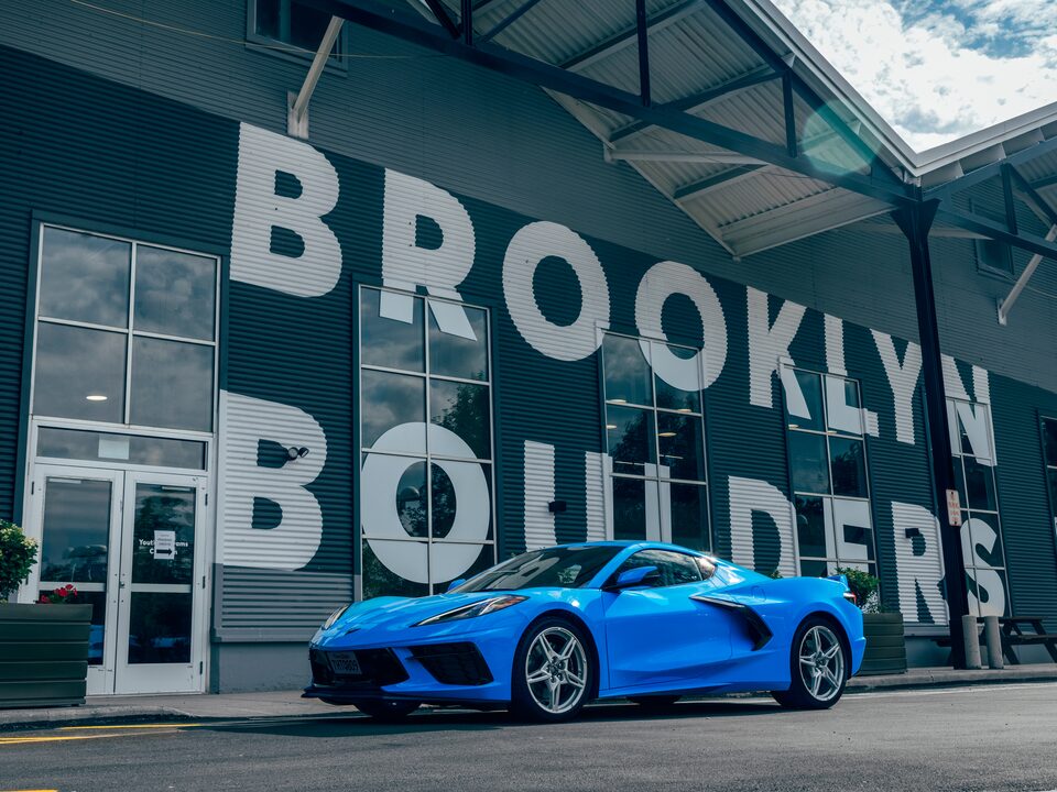 A bright blue 2020 Corvette sits on the street in front of a rock climbing gym with the name “Brooklyn Boulders” in huge white letters on the front of the building.