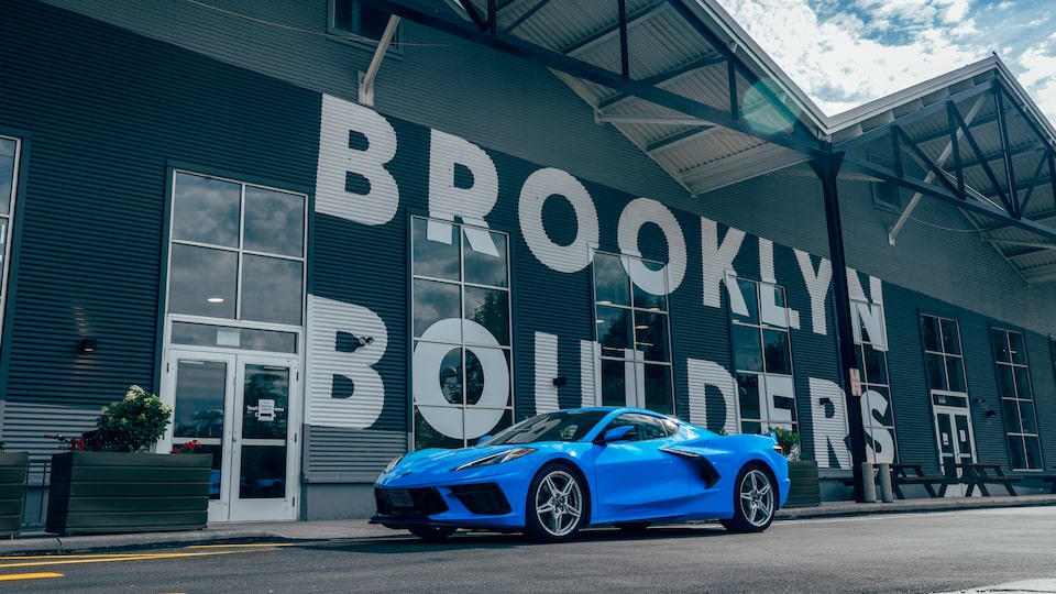 A bright blue 2020 Corvette sits on the street in front of a rock climbing gym with the name “Brooklyn Boulders” in huge white letters on the front of the building.